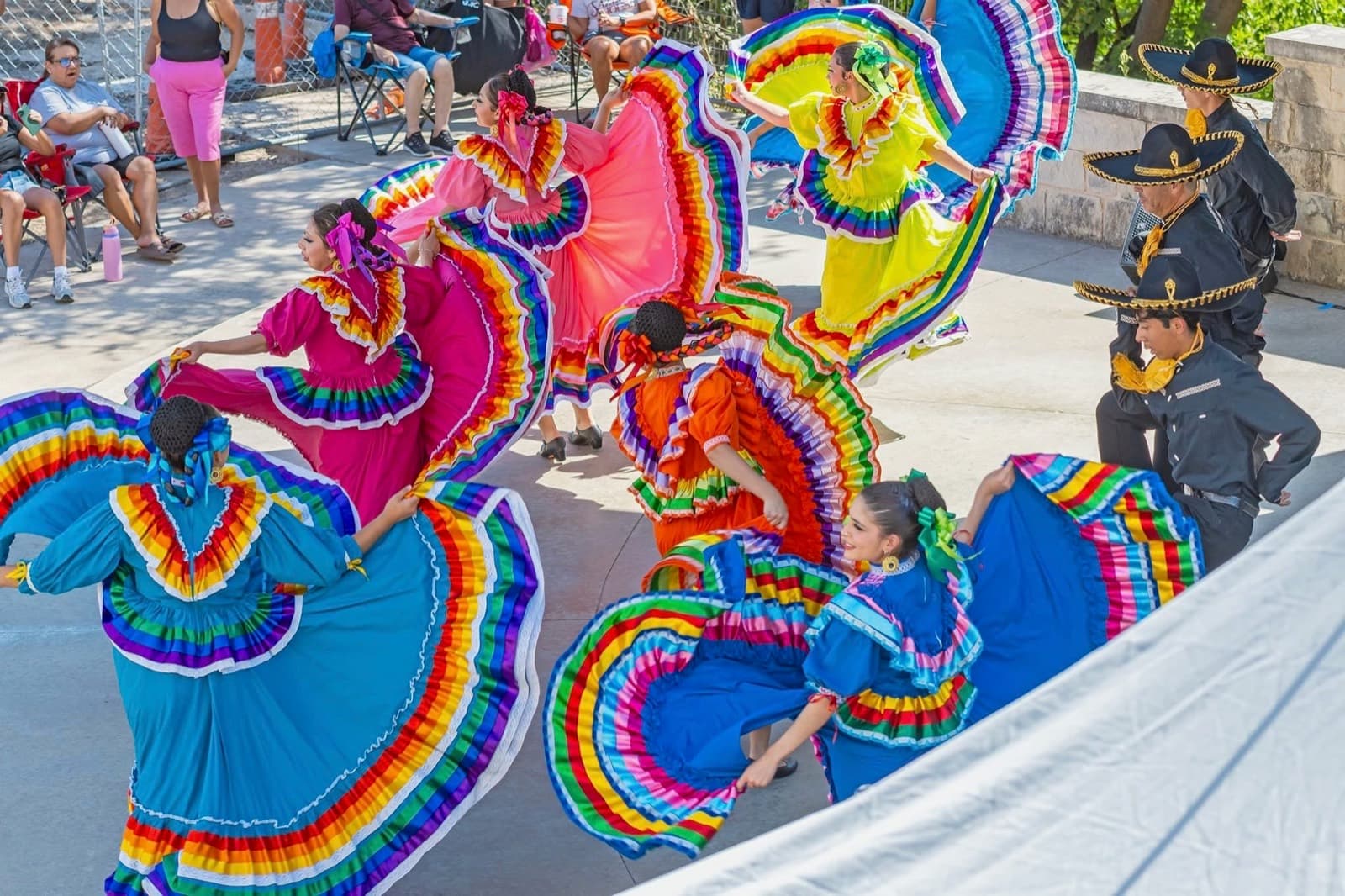 Round Rock Ballet Folklórico dancers swirling rainbow-ruffled Jalisco skirts at an outdoor performance